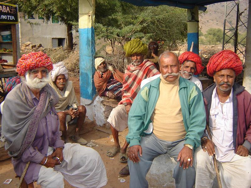 several people in different colored turbans outside and sitting down