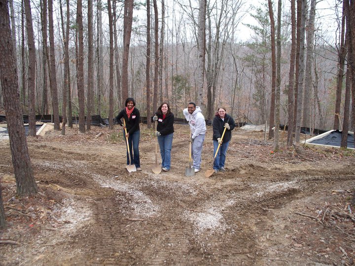 four people standing around in the woods with shovels