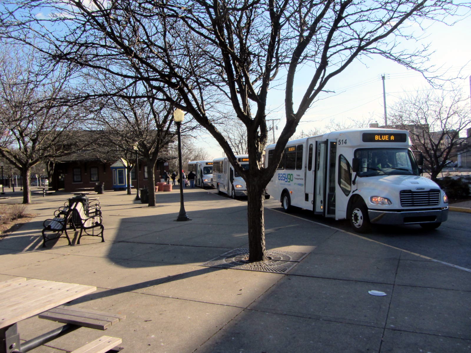 a white bus is parked in front of a bench