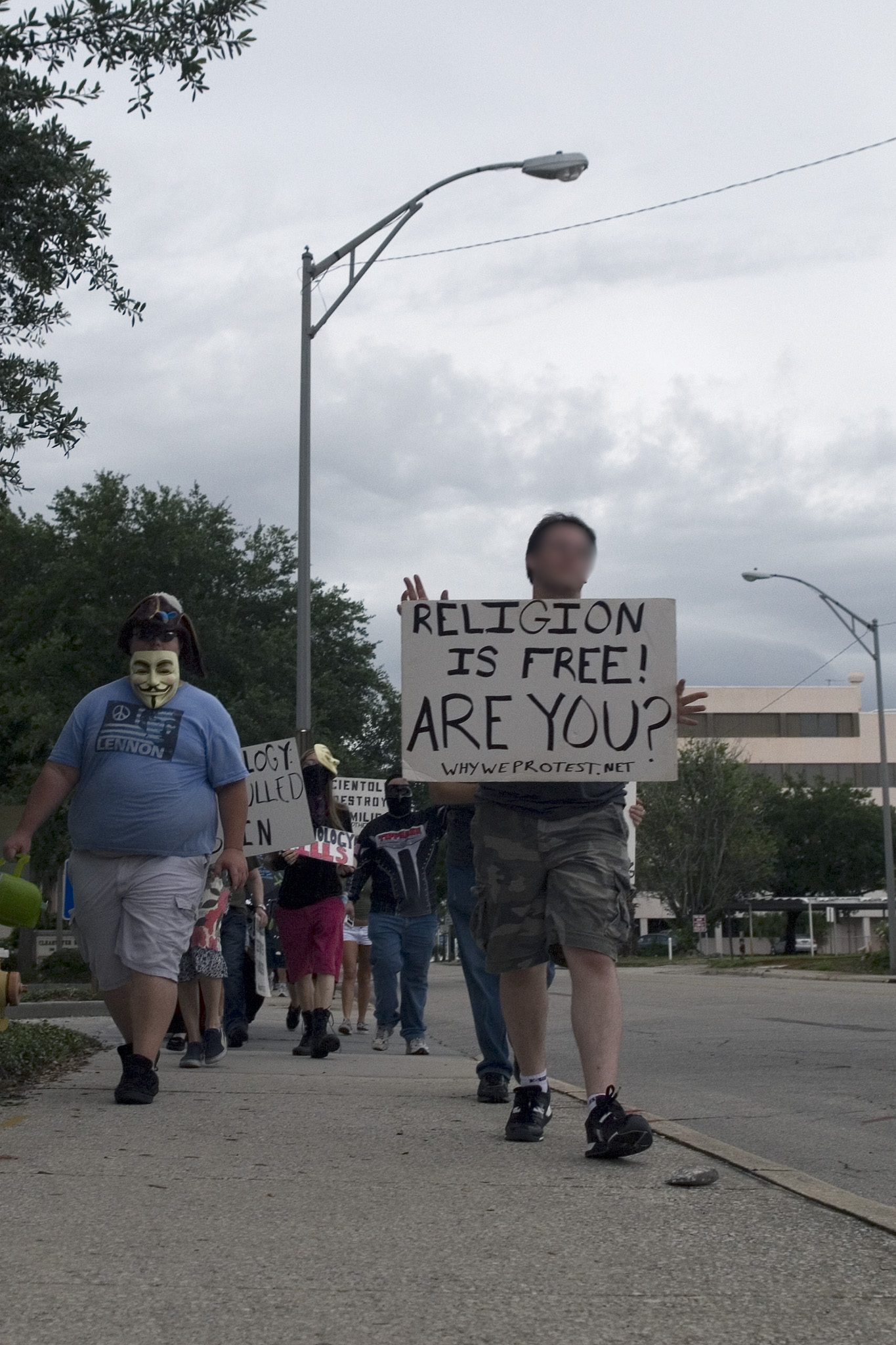 a man in a face mask is holding a sign as others walk down the road