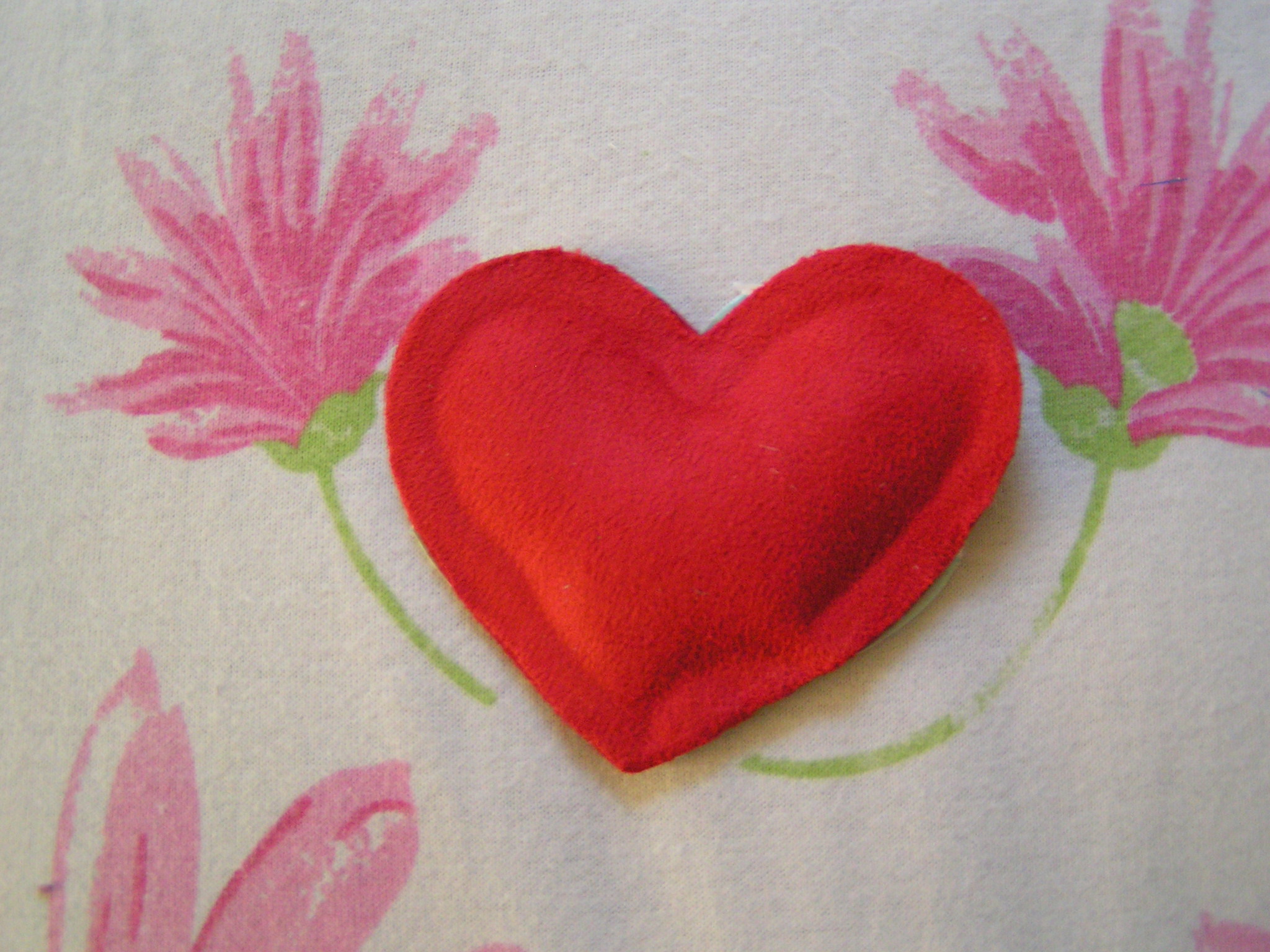 a red felt heart laying on top of a white fabric covered wall