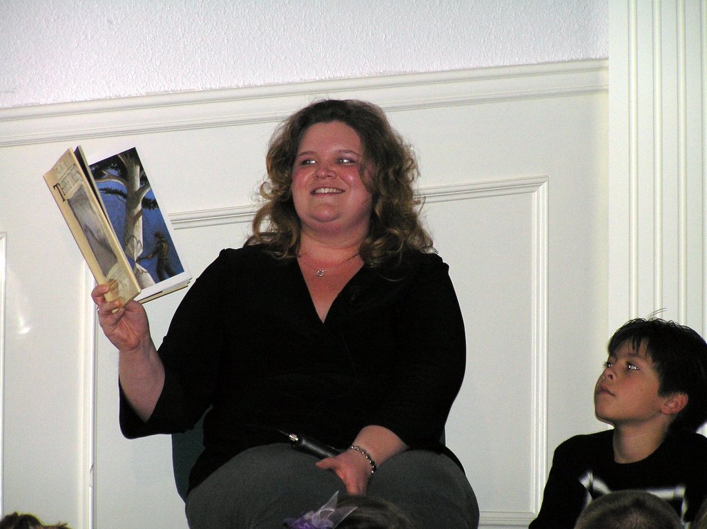 a woman holds a copy of an old paperback book while two children sit in the background