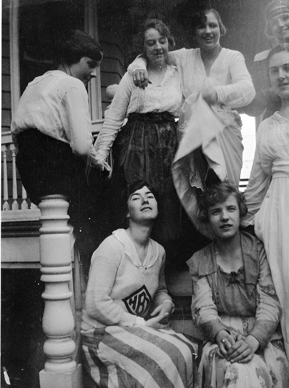 four women are posing on a porch, all one is dressed like a patriotic officer