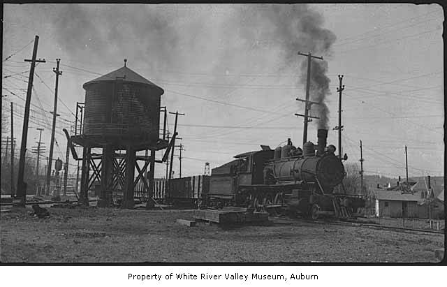 an old steam locomotive in front of two water towers