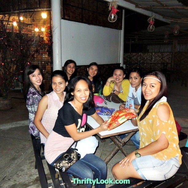 women smile for a group pograph while sitting at a table with some pizza