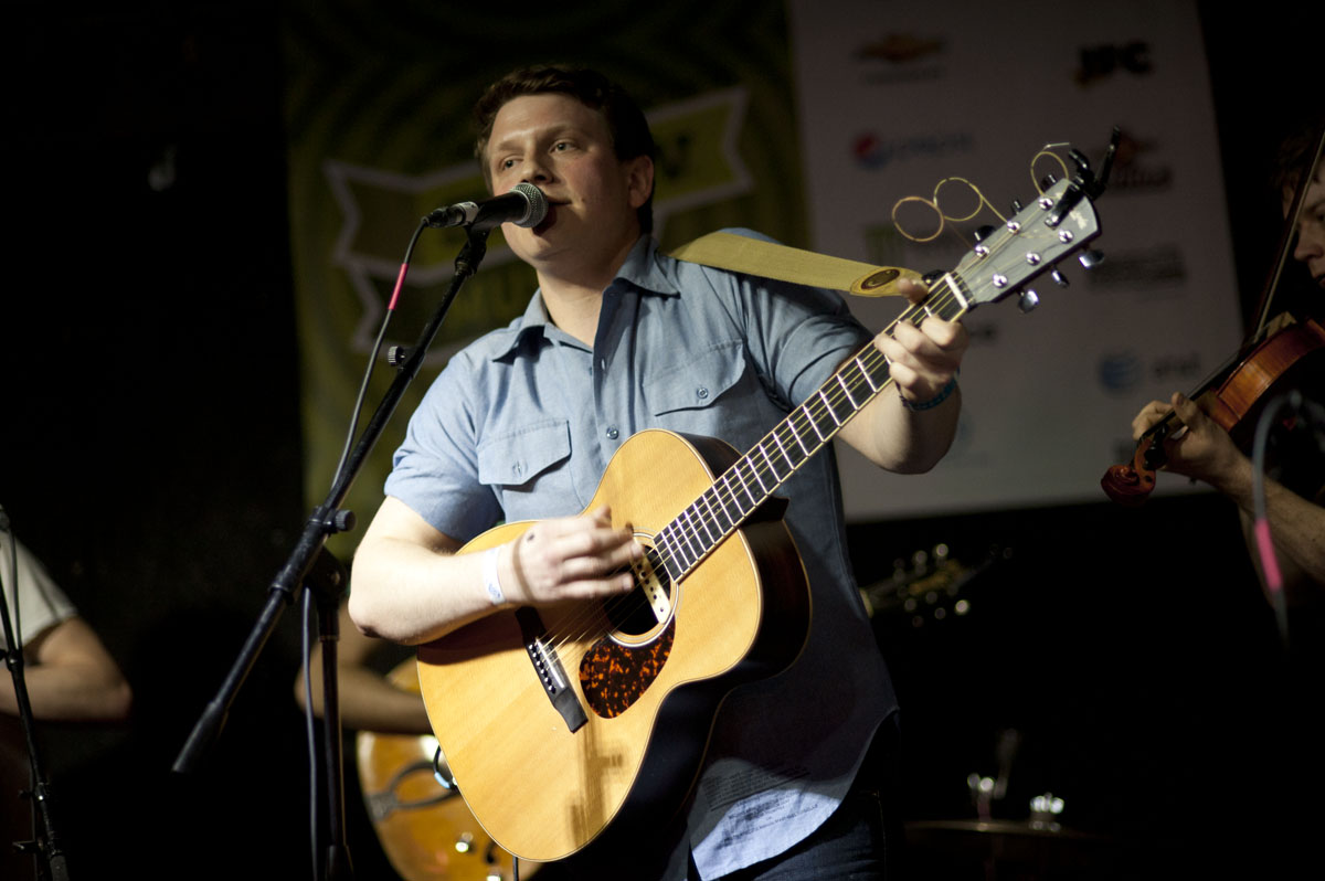 a man playing an acoustic guitar while standing in front of a microphone