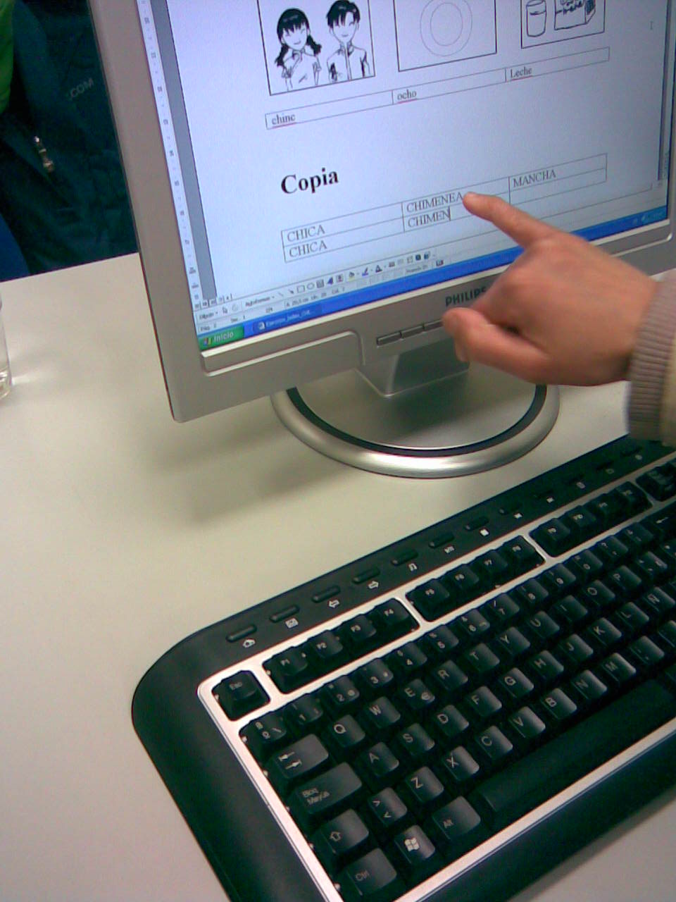 a keyboard and monitor on a desk with people in the background