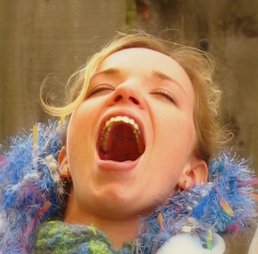 a person holding up an opened mouth and wearing a blue and green sweater