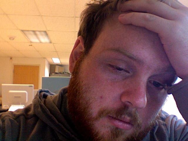 a bearded man in an office looks pensive