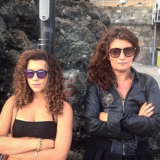 two woman standing next to a brick wall with their arms folded