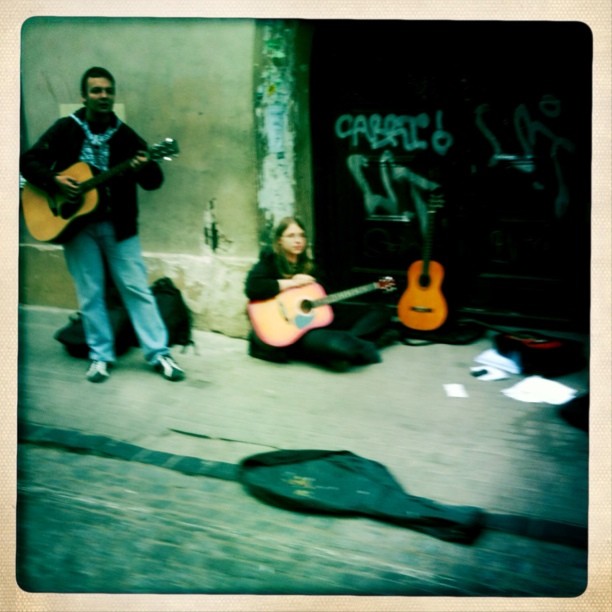 a girl holding a guitar, while another plays the instrument in the street