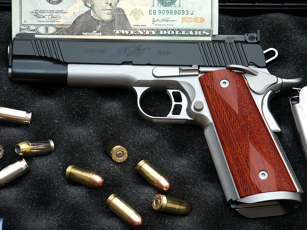 a handgun next to a money bill, which is placed on a bed of bullet shells
