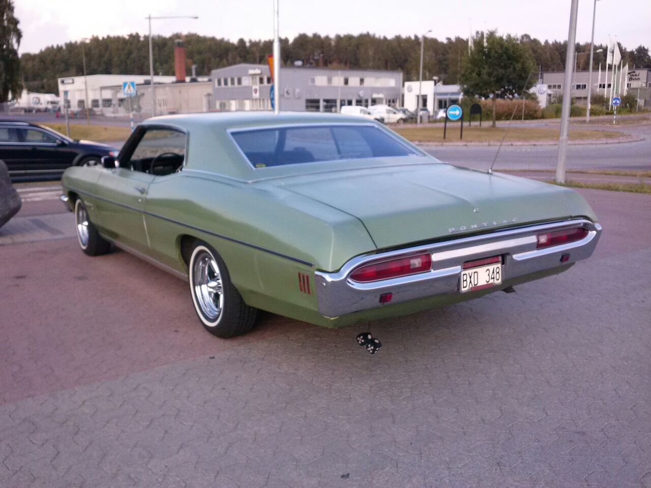 a green car parked on the pavement with other cars behind it