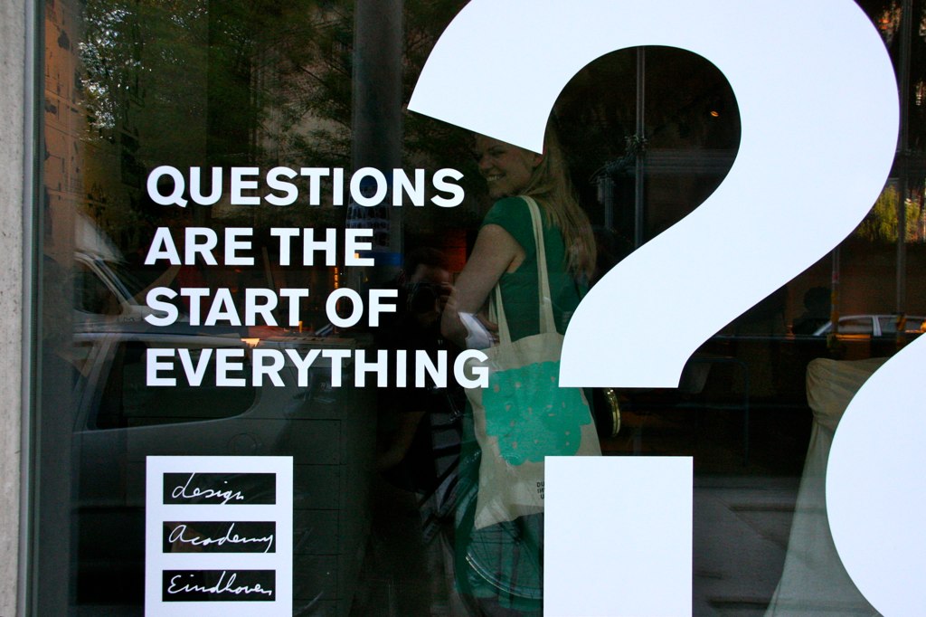 a person that is walking out of a building with an interesting question sign in the window