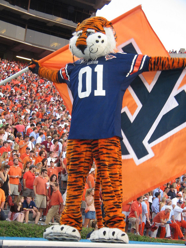 a man in tiger costume stands on a stage with a football player and flag