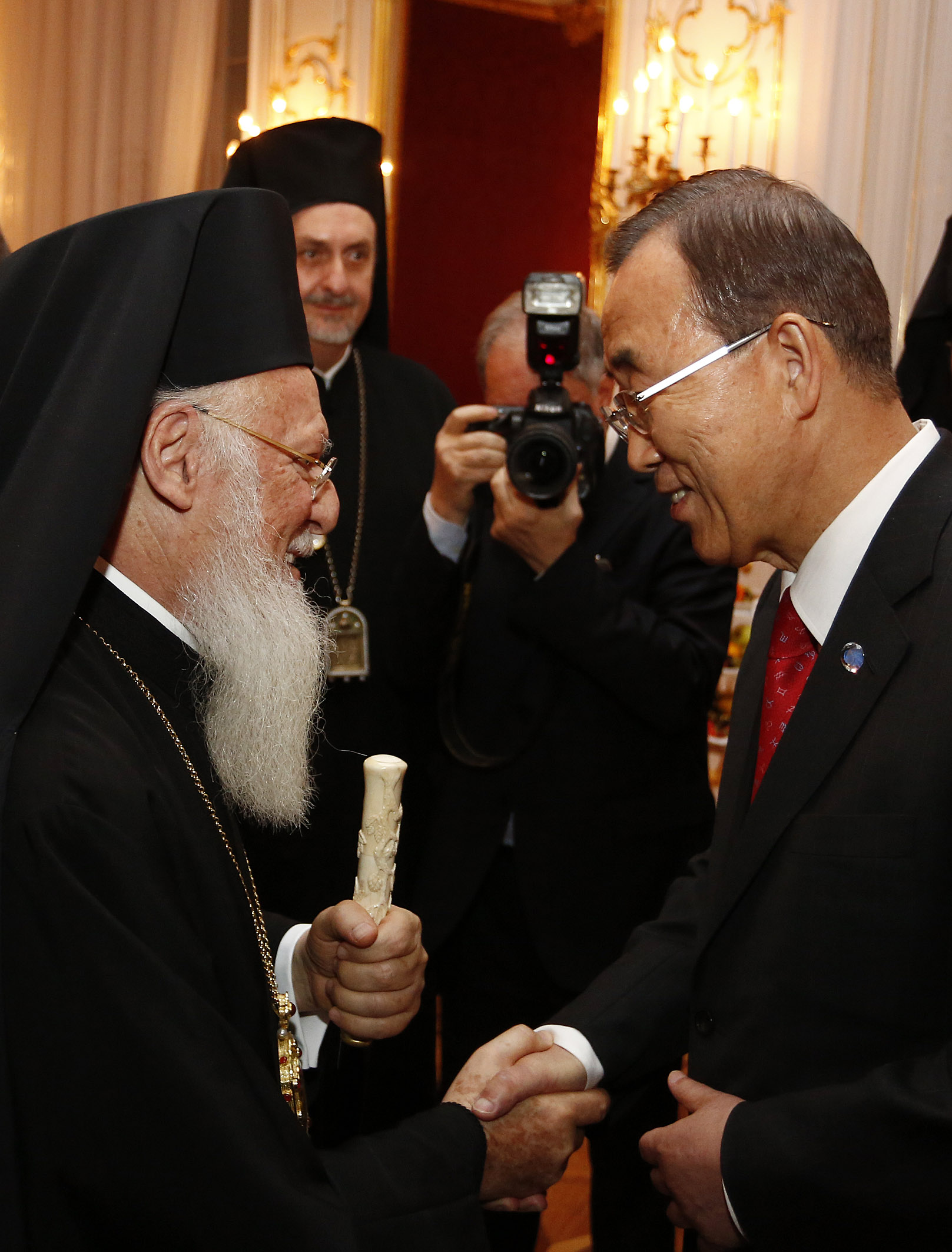 two men shaking hands, one wearing a religious garb and holding a bat