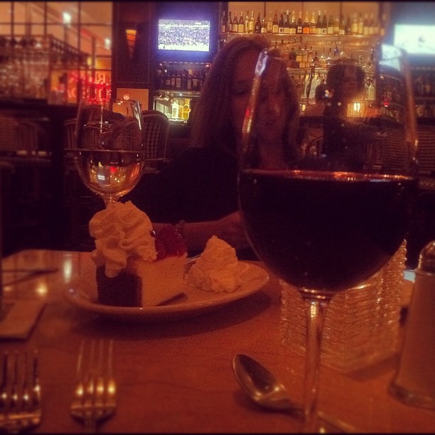 a person with their face next to a plate of dessert and wine glasses