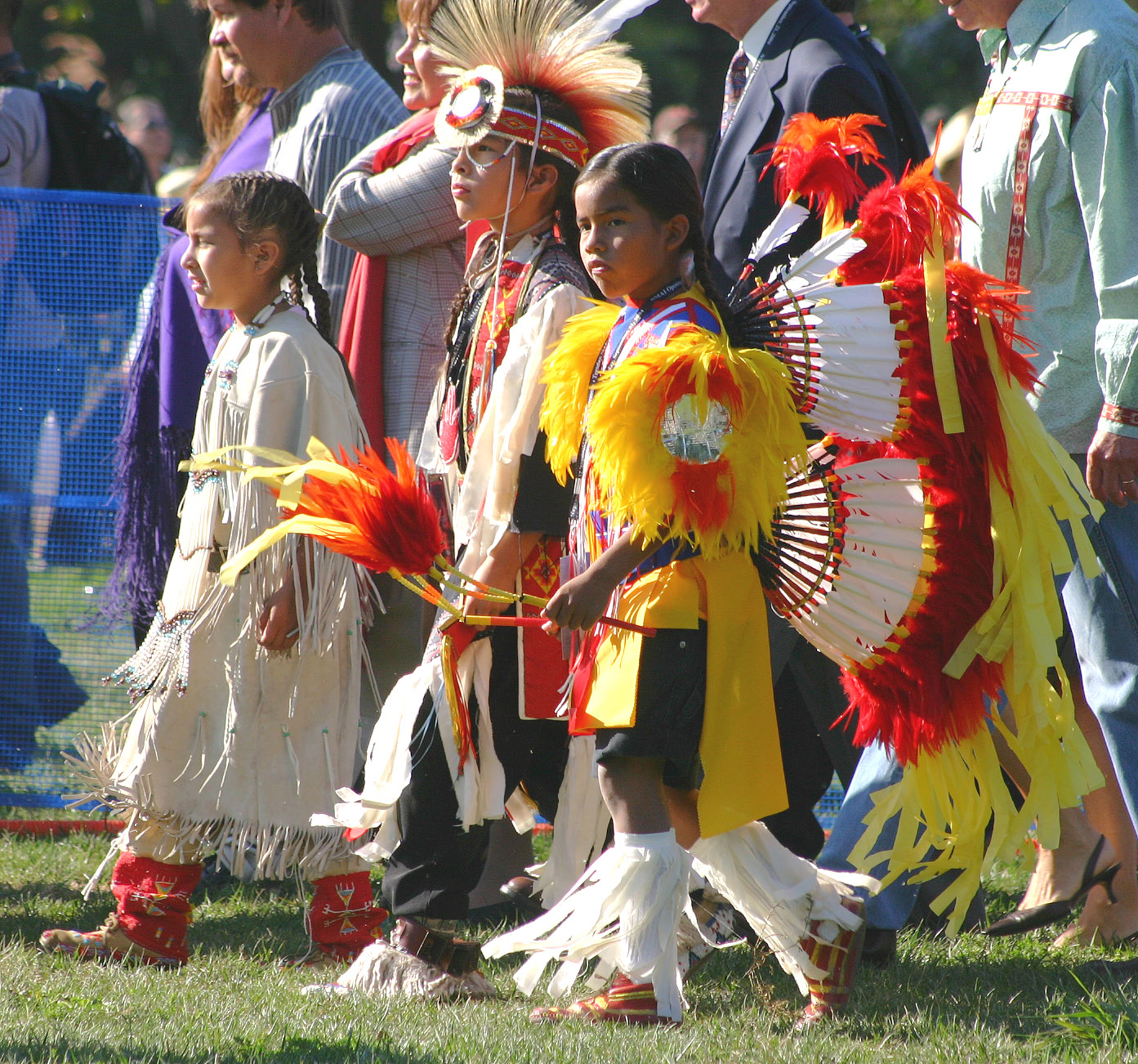 several people in native american costumes walking down the grass