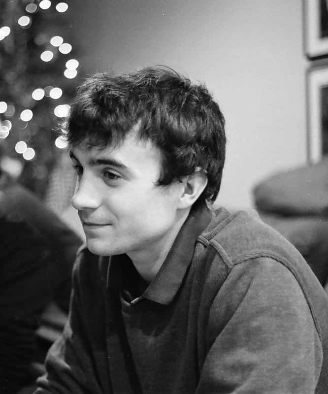 a black and white po of a man in a sweater sitting in front of a christmas tree