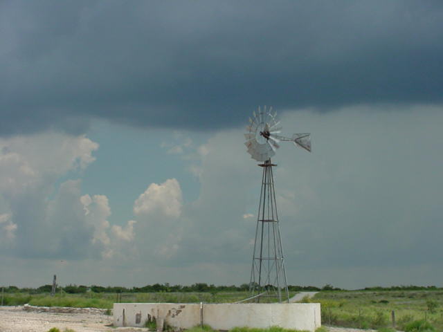 a windmill next to a farm with clouds