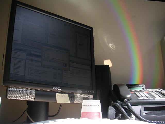 a desk with a computer and telephone and rainbow in the background
