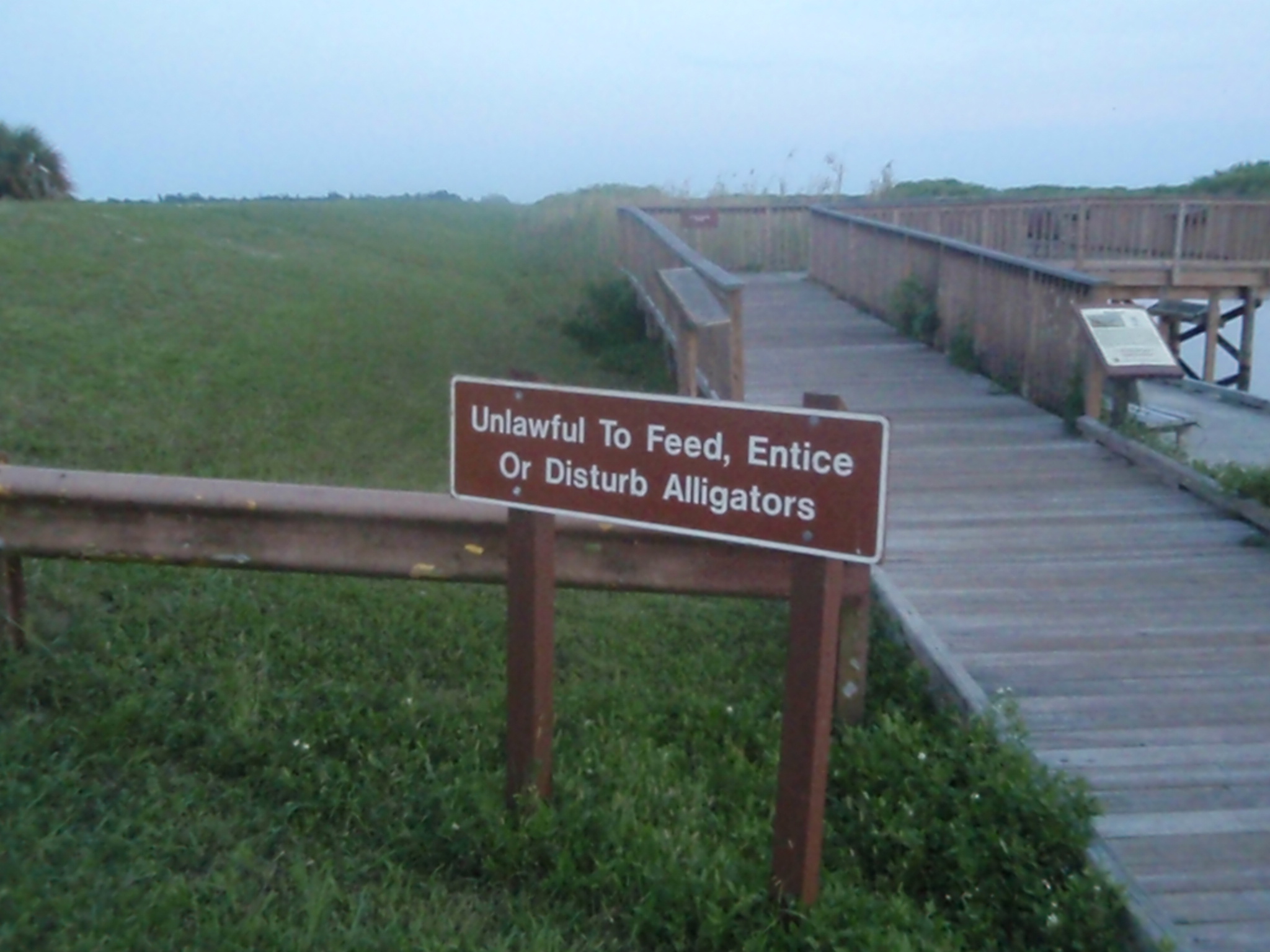 a sign by a wooden walkway that tells the distance