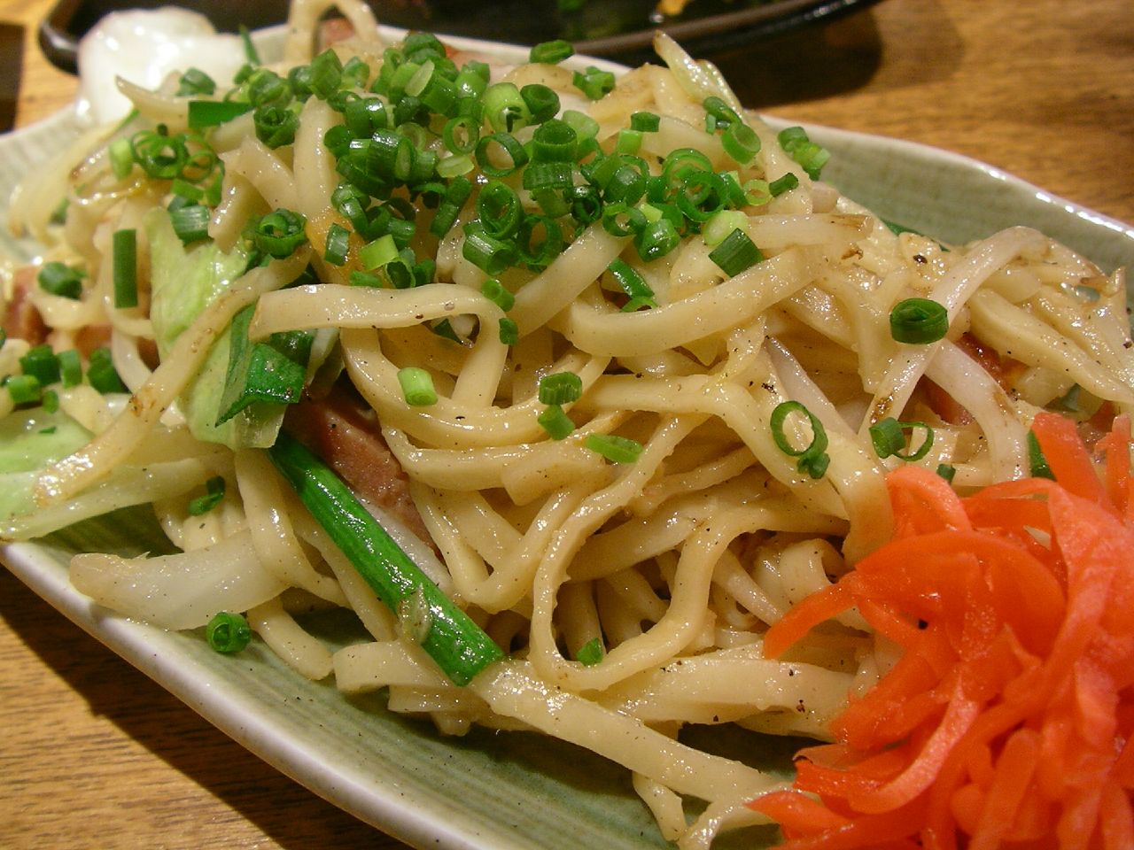 the plate of noodles is topped with meat, scallions and green onions