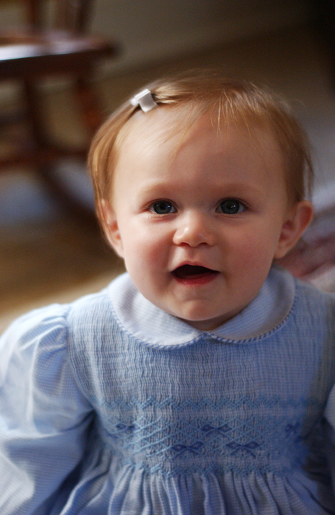 a toddler smiles at the camera in a blue dress