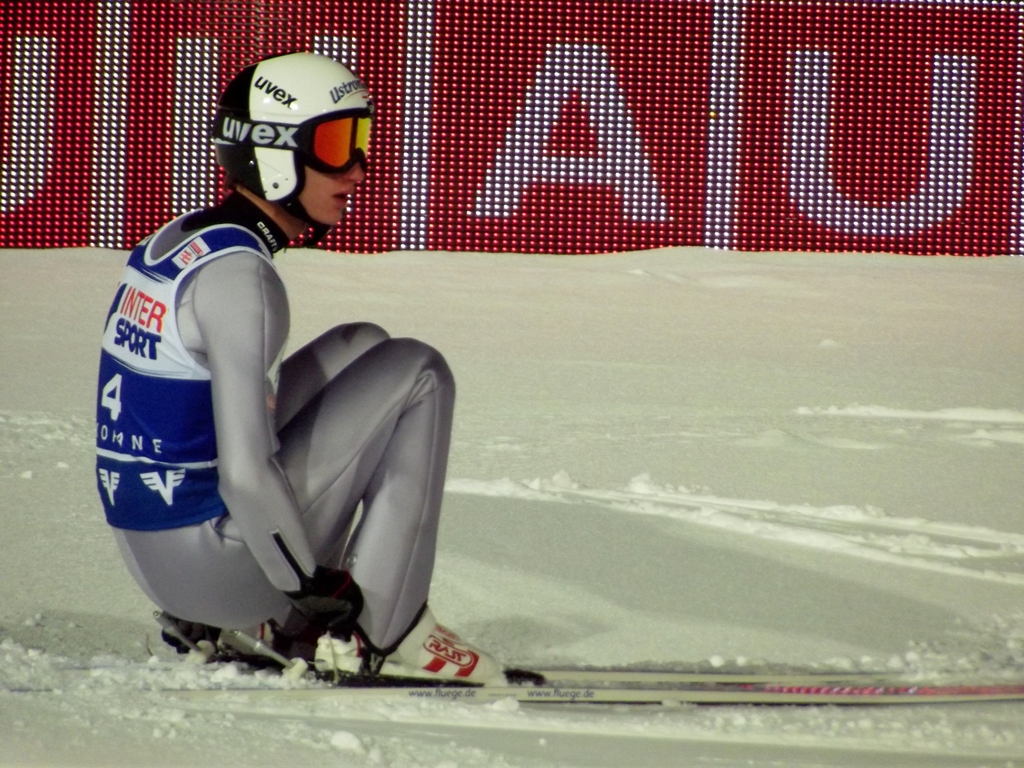 a skier crouching down wearing skis and an all - weather suit