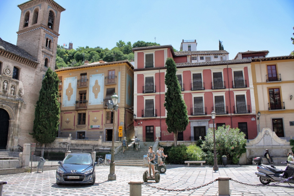 people and cars near a large building on a brick street