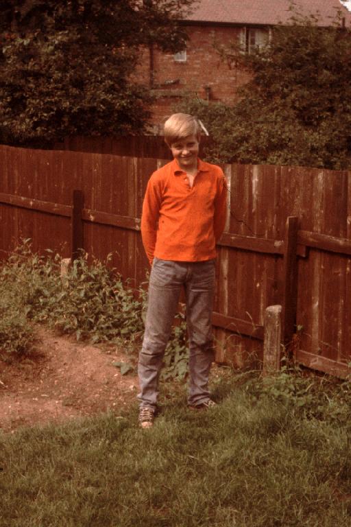 a young man standing in the yard next to a fence