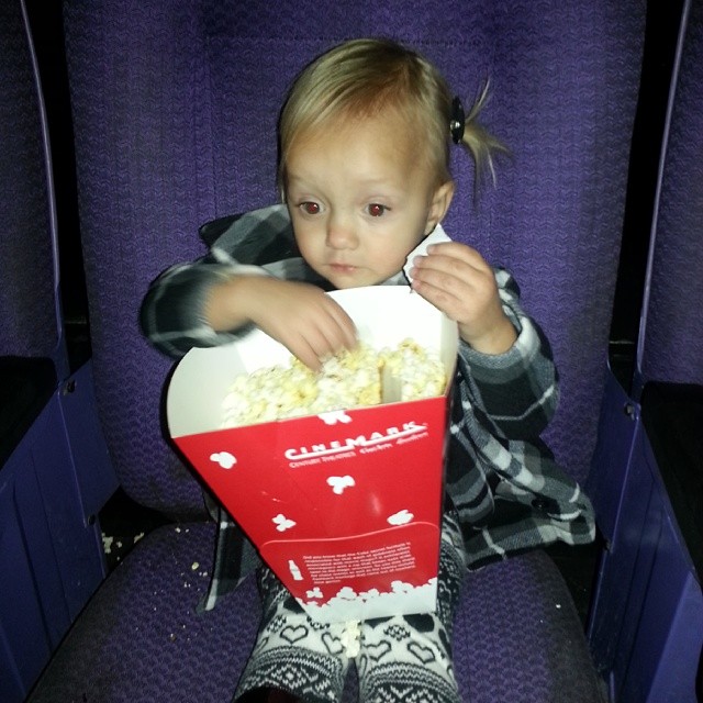 a small child sits on a bench holding a popcorn