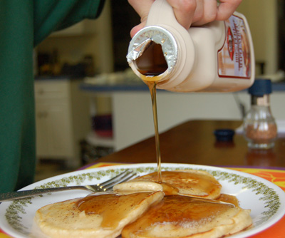 someone pouring syrup on some pancakes on a plate