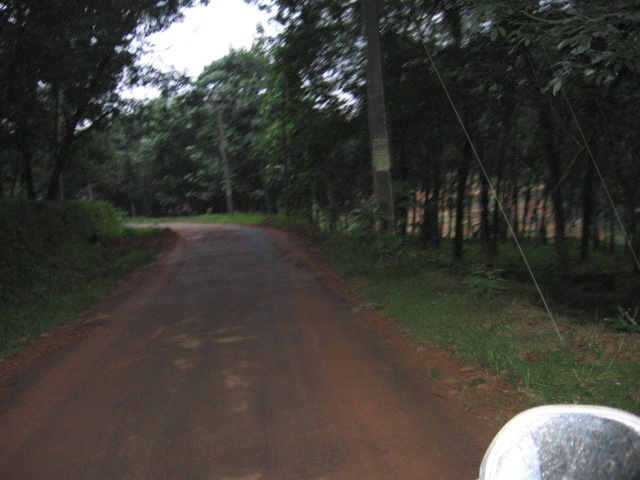 view from the inside of a car looking down a dirt road with a sign hanging from it