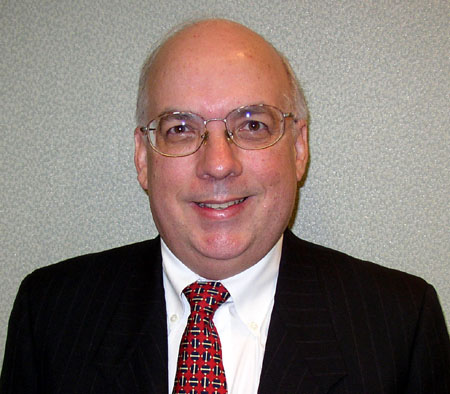 an older balding man in a black jacket with a red tie