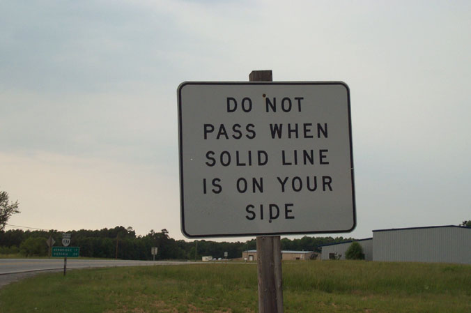 a white sign stating that the road pass when there is no line