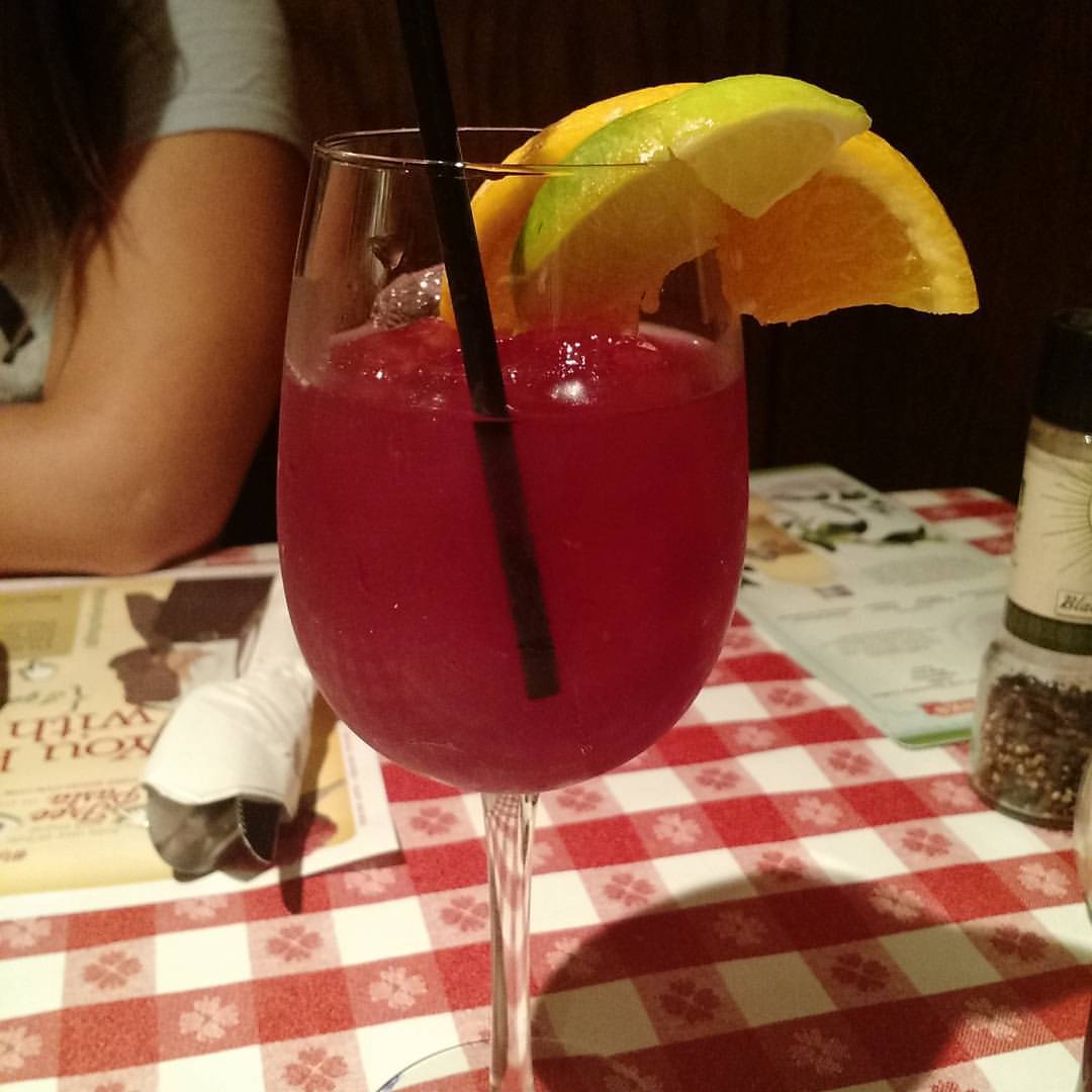 a red drink sitting in a wine glass with lemon wedges