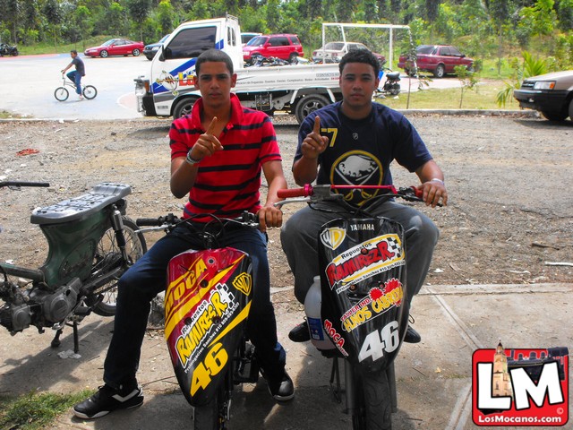 two young men riding motor bikes in parking lot