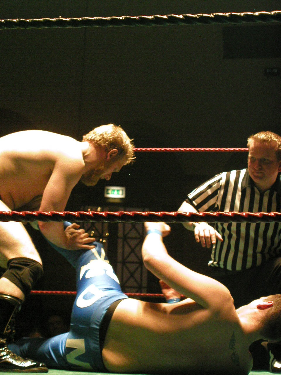a wrestling referee and a guy in the ring, with an referee standing behind him