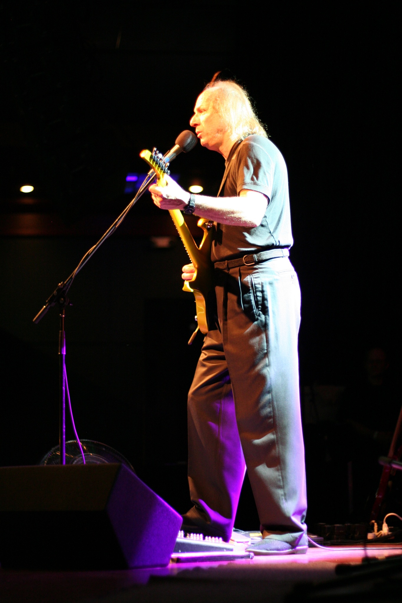 a man in overalls on a stage holding a microphone