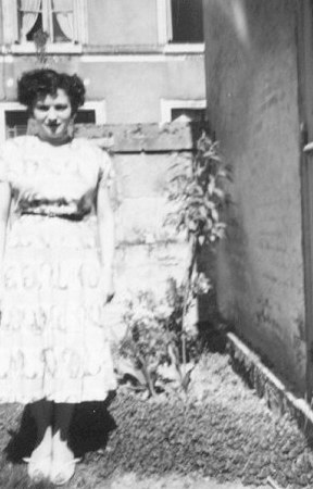 an old picture of a young woman standing in front of a house