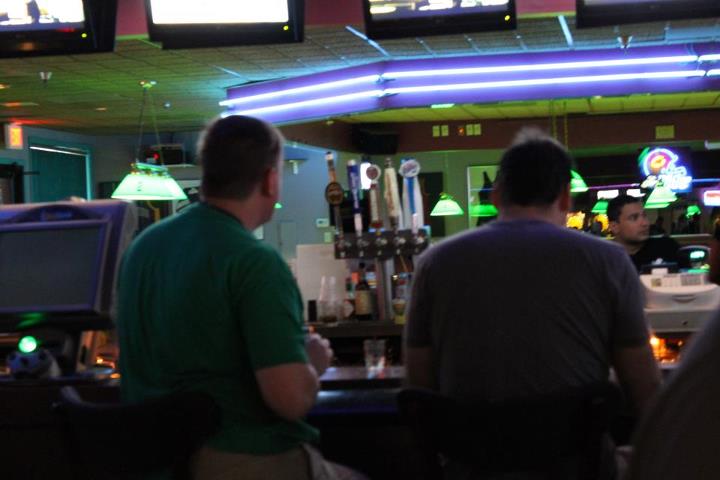 men sitting at a bar playing a game on tv screens