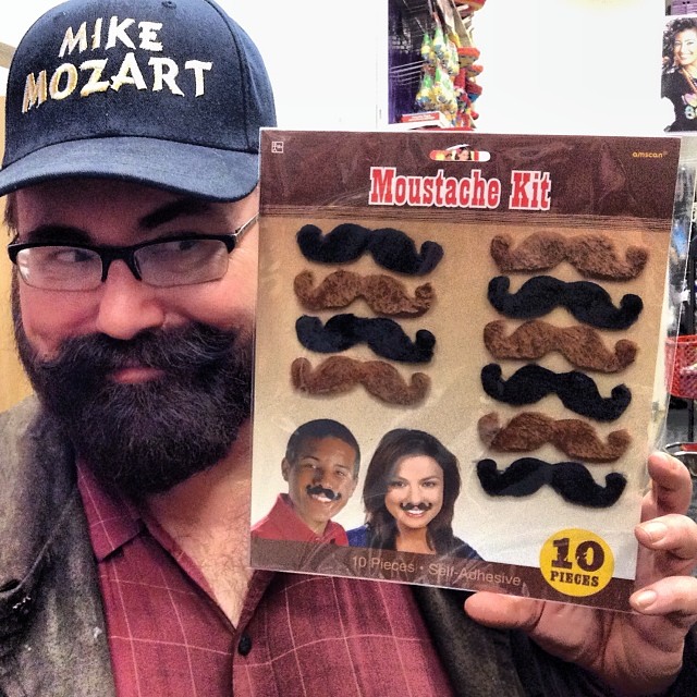 a bearded man is holding a package of fake mustache kits
