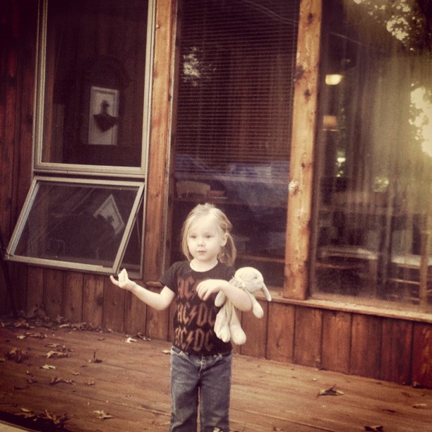 a little girl holding a stuffed animal standing on a porch