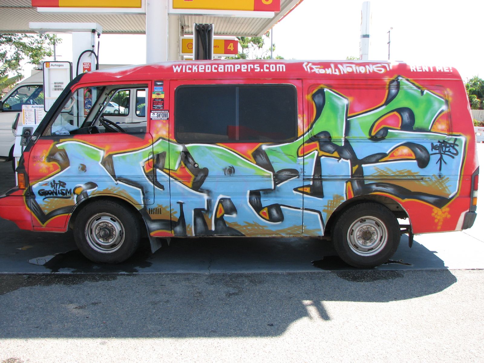 a colorful bus painted to resemble graffiti sitting next to a gas station