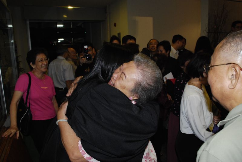 an elderly man wearing a black neck gard hugs a woman