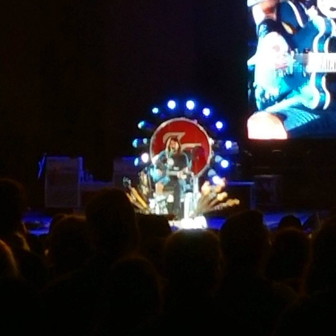 a man playing the guitar on stage with a large television in the background