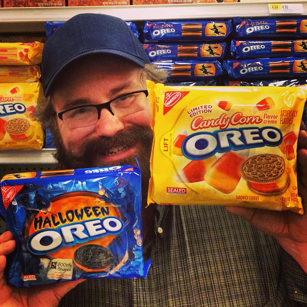a man holds two bags of halloween oreos and a package of candy