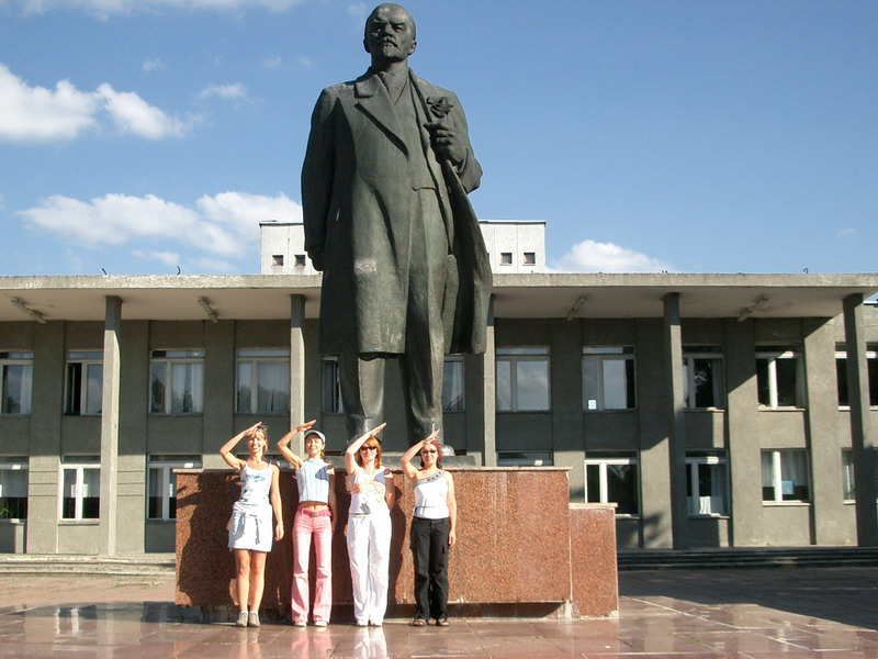 four women pose beside a monument with a statue in the background