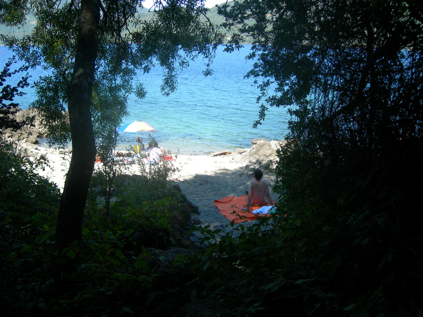 a woman sits on an orange beach towel looking out at the ocean